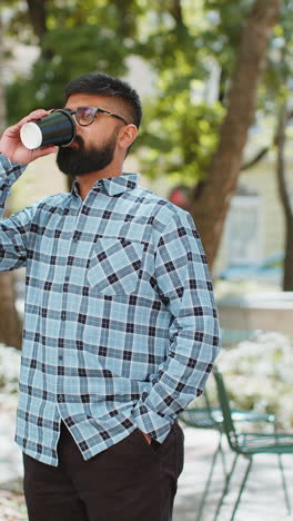 happy indian man enjoying drinking morning coffee hot drink relaxing taking a break on city street