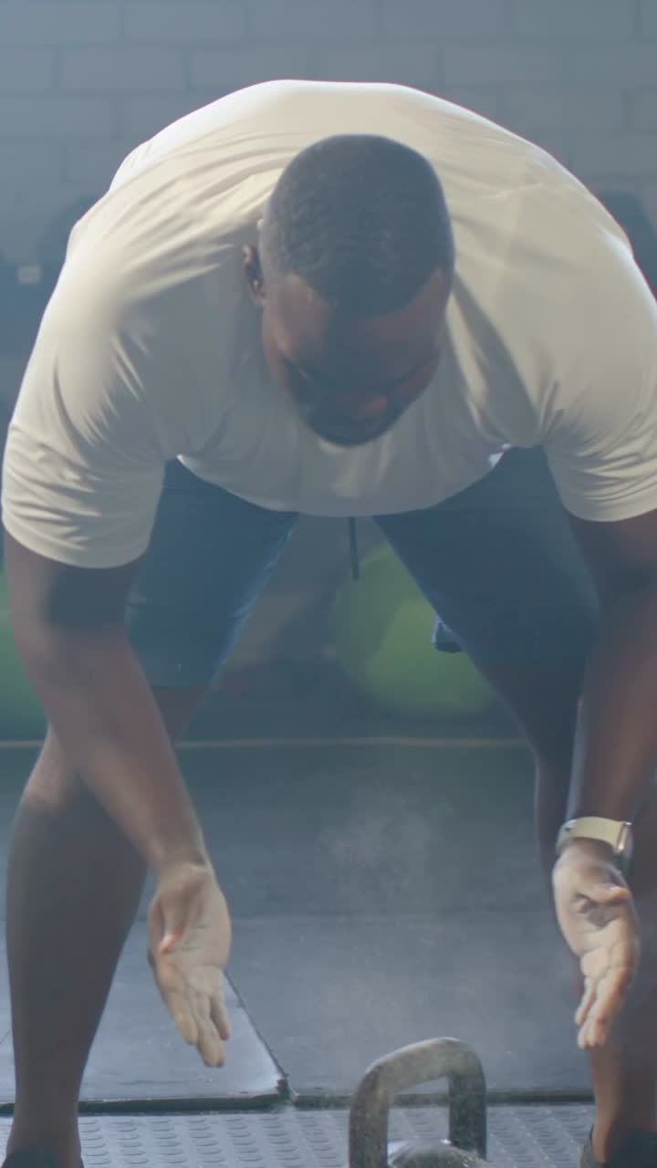Video verticale: Uomo in maglietta bianca che usa la magnesite, afferra un kettlebell in palestra preparandosi a un sollevamento, polvere di magnesite.