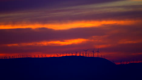 Moderne-Industrie-Und-Natur-Stehen-Im-Einklang,-Während-Windturbinen-Während-Eines-Pulsierenden-Sonnenuntergangs-Saubere-Energie-Erzeugen---Zeitlupe