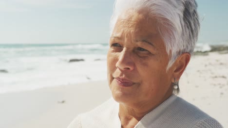 Portrait-of-thoughtful-senior-hispanic-woman-standing-on-beach-and-look-into-distance