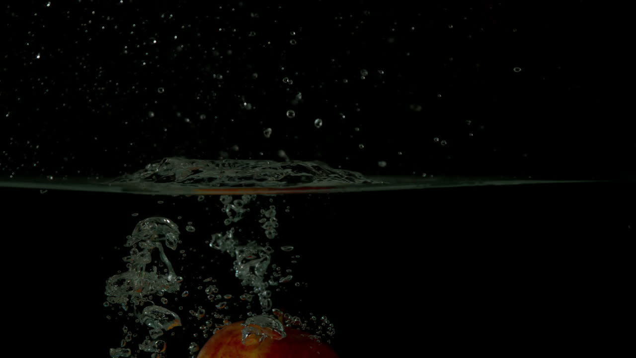 manzana roja sumergiéndose en el agua sobre un fondo negro