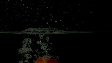 Red-apple-plunging-into-water-on-black-background