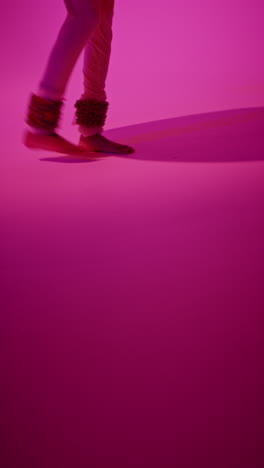 vertical video close up of feet with bells of female kathak dancer performing dance wearing traditional indian dress against purple background