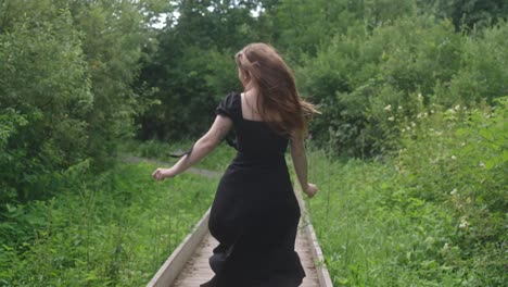 woman in black dress walking on a wooden boardwalk in a lush green park