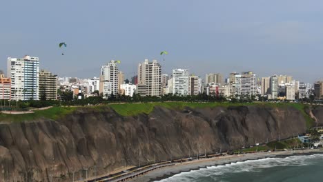 Paragliders-flying-like-birds-over-the-coastline-of-the-Lima-capital-city,-in-Peru,-the-Miraflores-district