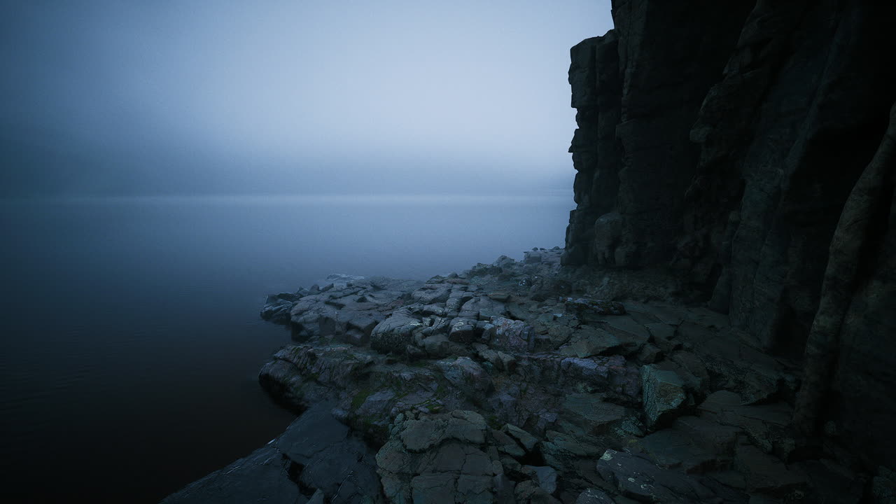 Calm waters reflect mysterious fog over rocky shoreline at dawn