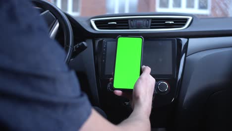 un conductor masculino usa un teléfono inteligente verticalmente con una pantalla verde, sostiene un teléfono en la mano. maqueta para un navegador o aplicación de carretera. se aleja, elimina el mapa. construye una ruta en un mapa de la ciudad