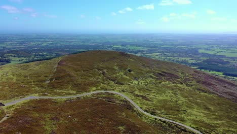aerial view of road crossing hilltop with a forest and view into the distance in the background during summertime in the south of ireland
