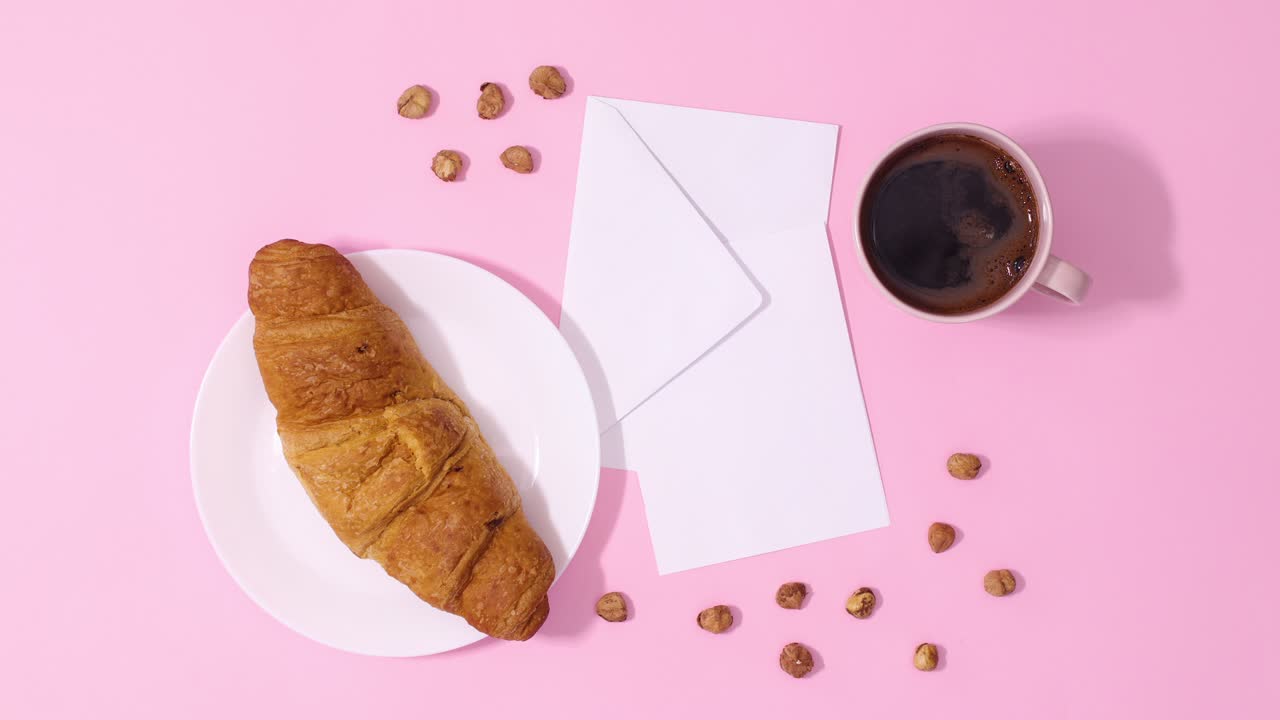 croissant fresco y una taza de café aparecen con una nota de tarjeta de papel en un fondo rosa pastel. detenga el movimiento
