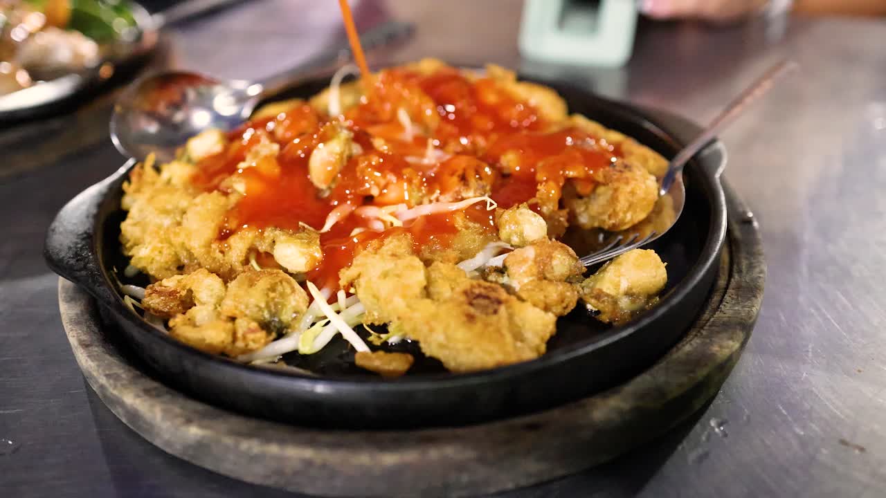 Hot sauce poured onto crispy oyster pancake on sizzling plate, vibrant street food market lighting