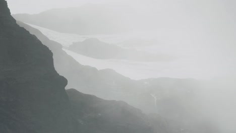 clouds rolling over snow and a waterfall on mountain top