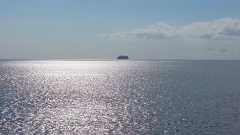 Panorámica-Aérea-De-Camiones-A-Través-De-Brillantes-Aguas-Del-Océano-Con-Un-Crucero-En-La-Silueta-Del-Horizonte