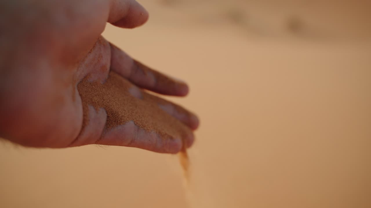 Close-up of a hand releasing fine orange sand in the dunes of Merzouga, Sahara Desert, Morocco