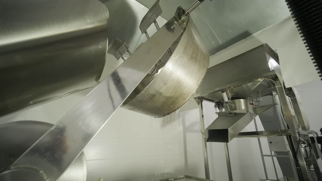 producción de papas fritas y bocadillos. máquina industrial de fritura profunda. las papas fritas se fríen en un cuenco grande con aceite. la línea de producción de la fábrica mueve las papas frias doradas después de freír.