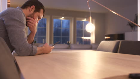 man sits at indoor table anxiously reading cell phone with distressed mannerisms