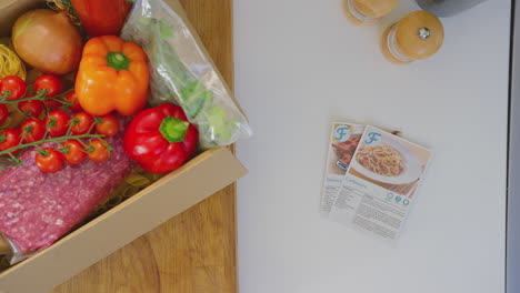 overhead shot of box of fresh ingredients next to recipe cards in kitchen - shot in slow motion