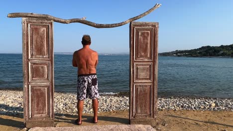 decorative seaside wooden door and back view of man standing in swimwear leaning against doorframe