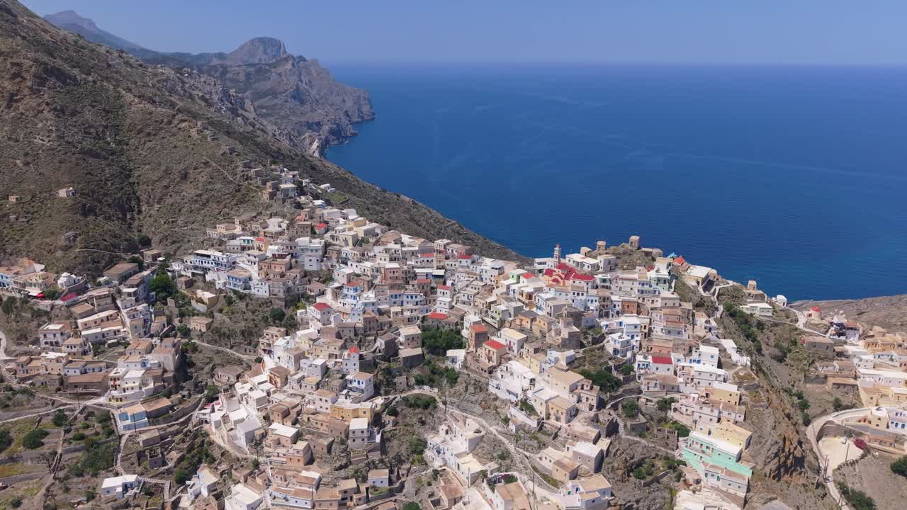 Panoramic drone footage capturing the traditional Olympos village in Karpathos, highlighting the hillside location, colorful houses, and the stunning surrounding Aegean landscape