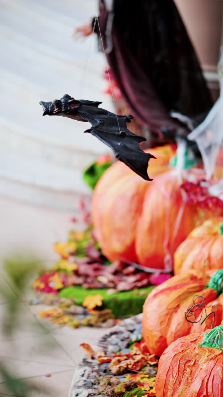 A bat figurine suspended above halloween decorations of pumpkins and spider webs. Vertical