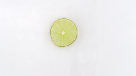 On-a-white-background-cut-into-slices-of-lime-sprinkled-with-water-spray.-Juicy-fresh-lime-in-slow-motion.