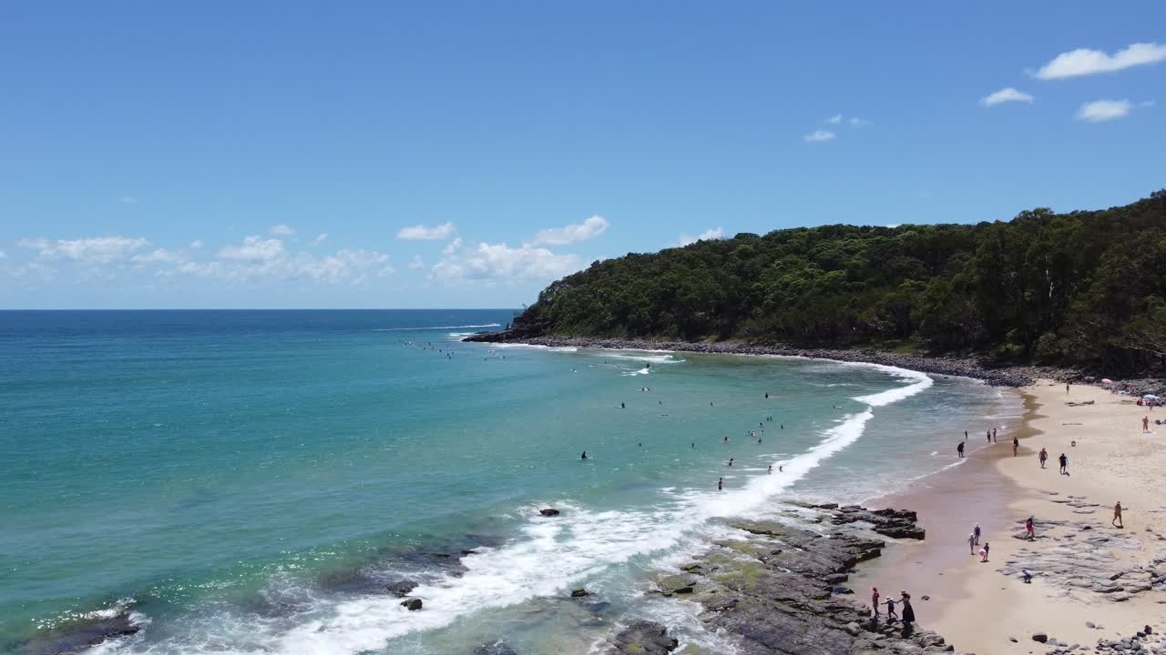 drone ascendiendo en una hermosa playa con surfistas en el fondo