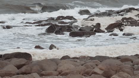 la espuma marina en cámara lenta sopla a través de una playa rocosa mientras las olas se agitan en el fondo