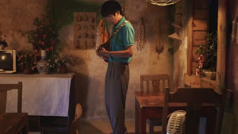 Young-Asian-male-playing-a-guitar-while-walking-around-a-rustic-room