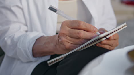 senior woman hands writing in notebook outdoors close up. old lady holding pen