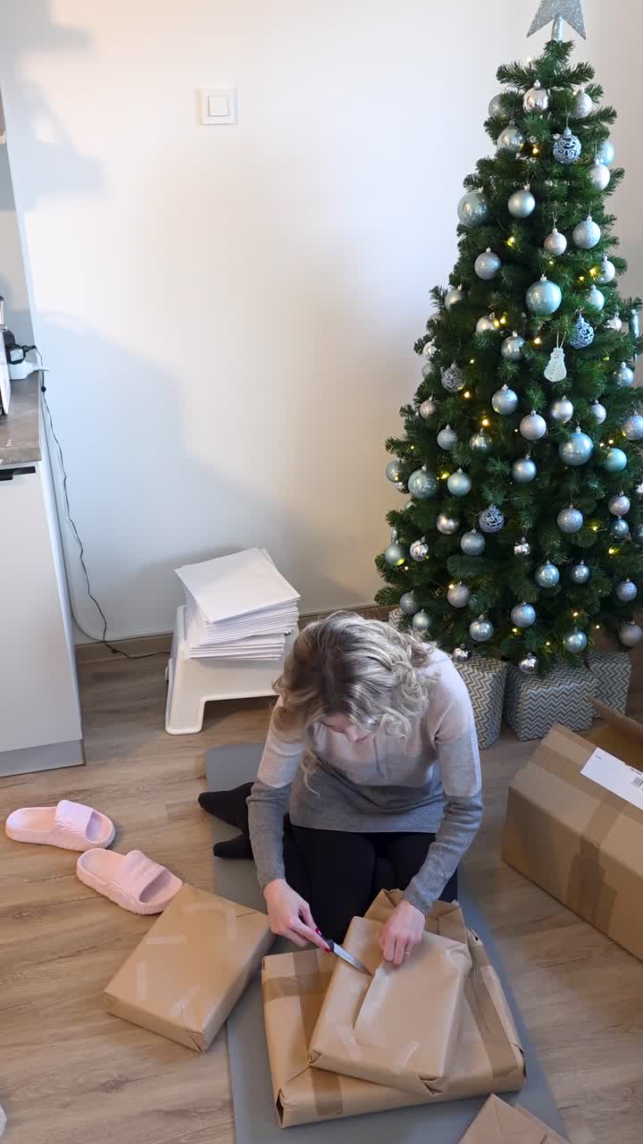 Inquadratura verticale medio-ampia di una donna che scarta un regalo sotto l'albero di Natale