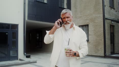 senior man talking on phone and drinking beverage outside