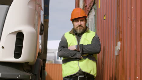 Worker-Wearing-Vest-And-Safety-Helmet-Looking-At-Camera-In-A-Logistics-Park