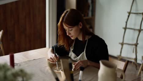 a red-haired girl potter varnishes a piece of clay with a special brush