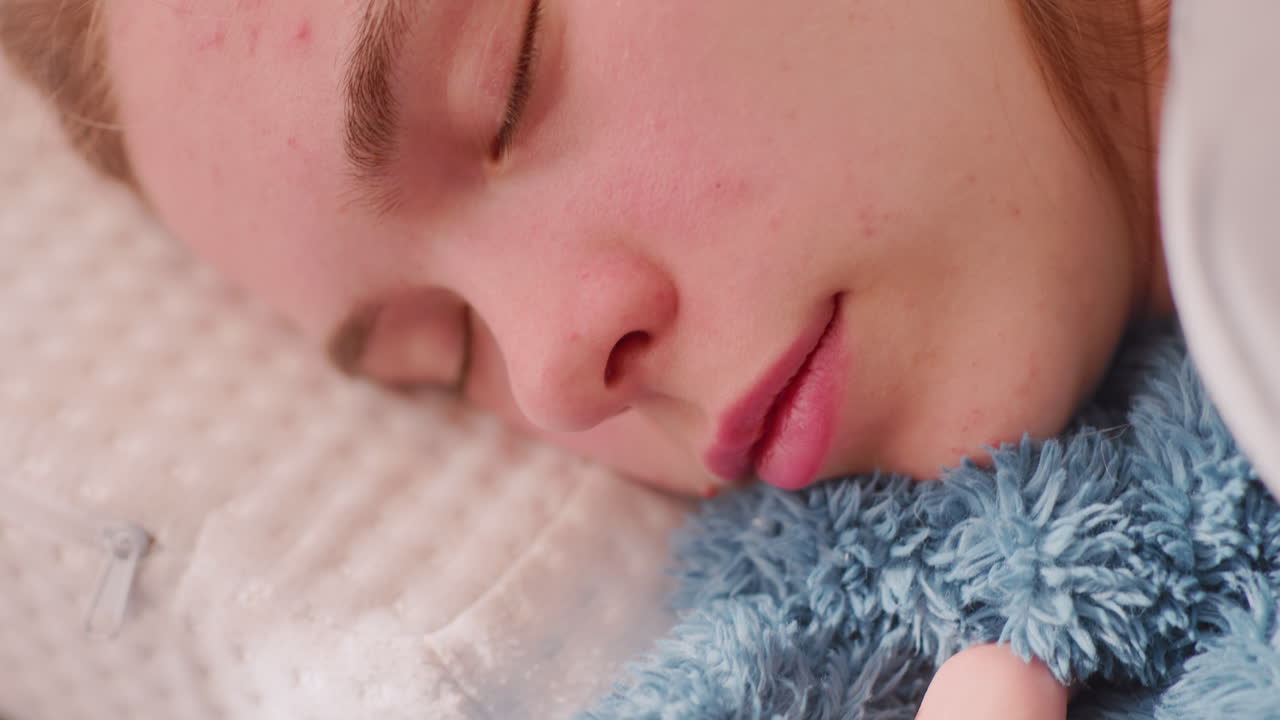 Close up of sleeping girl holding fluffy blue blanket closely while resting on soft pillow, symbolizing comfort, relaxation, coziness, warmth, and peaceful rest in serene indoor atmosphere