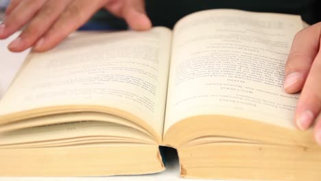 estudiante de sexo masculino leyendo un libro sentado entre pilas de libros