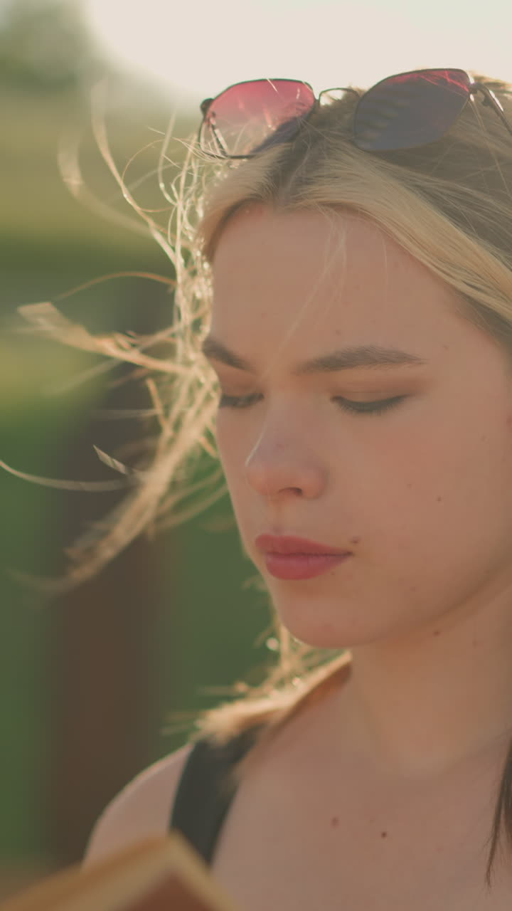 la mujer cierra el libro en su mano, toma una respiración profunda, como el viento sopla su cabello, el sol irradia en su rostro, y ella mira en la distancia, con la estructura de madera en el fondo