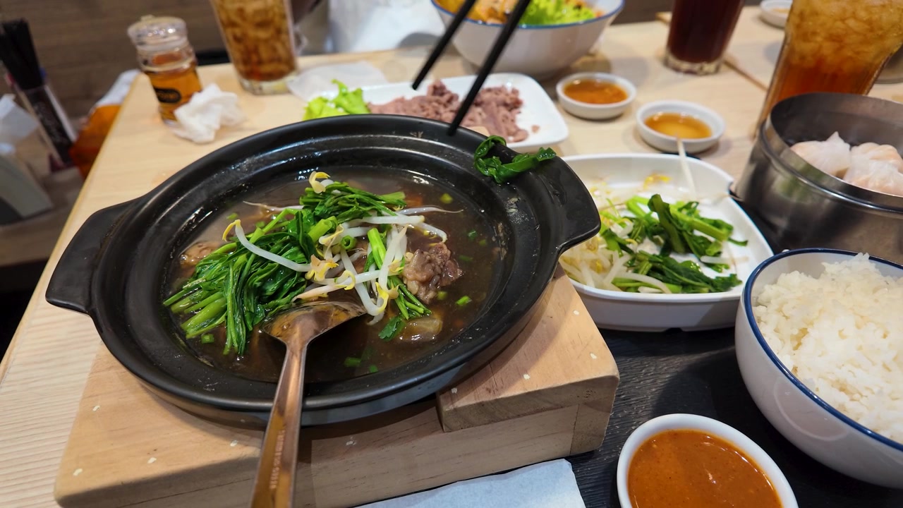 Palillos colocando verduras verdes en una olla de barro humeante con estofado de ternera en Bangkok, Tailandia.
