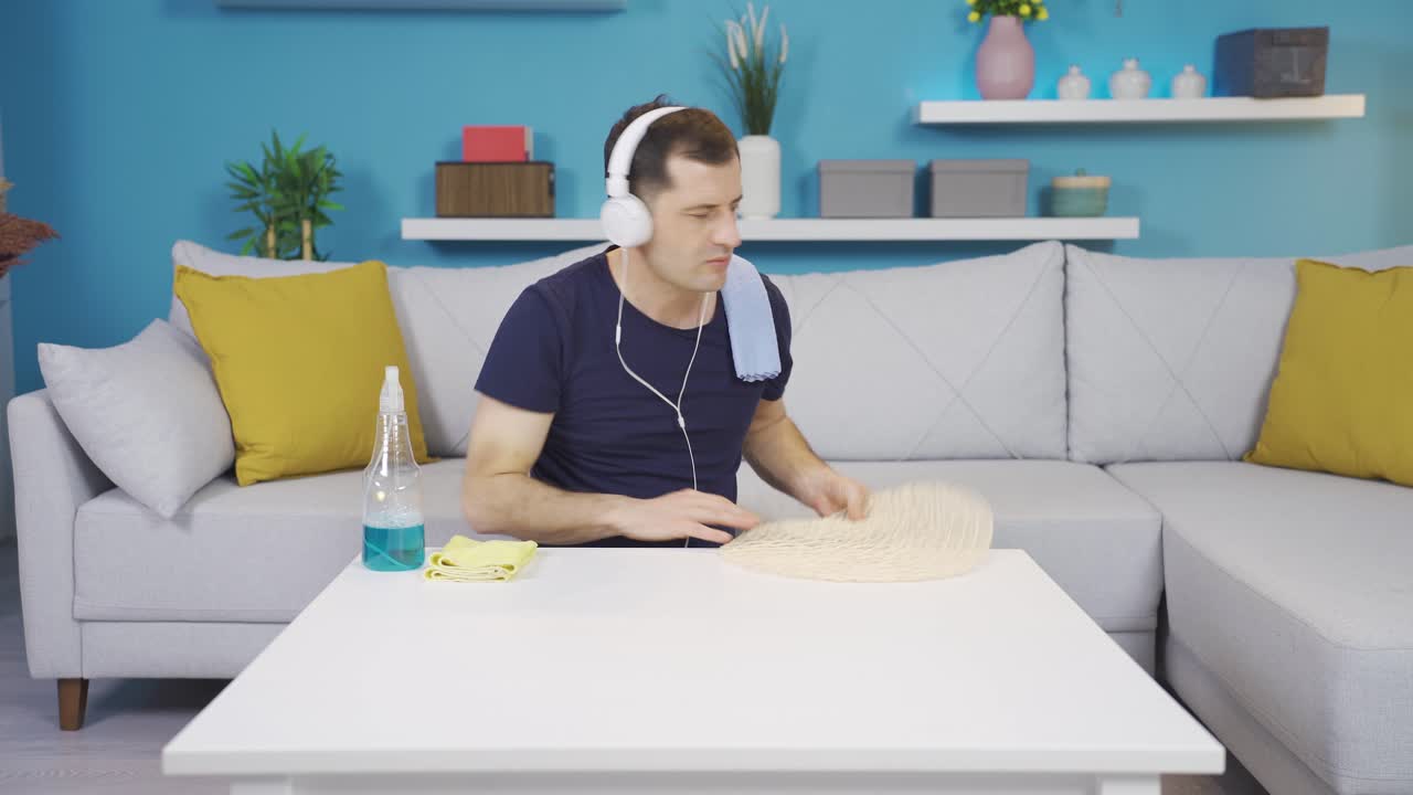 음악을 듣는 동안 청소하는 남자는 커피 테이블에서 물건을 제거하고 테이블을 청소합니다.