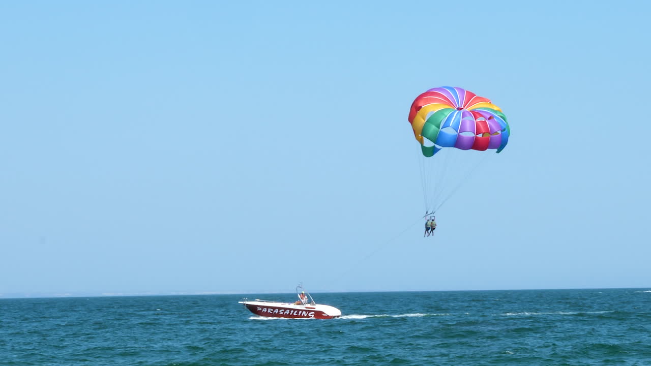 Two people in the air parasailing getting down from the air in the boat