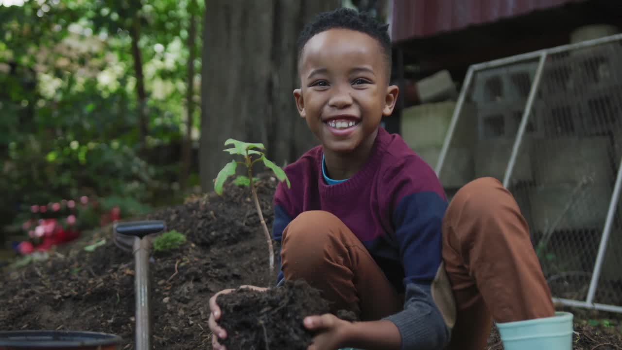 retrato de un feliz niño afroamericano sosteniendo una planta en el jardín