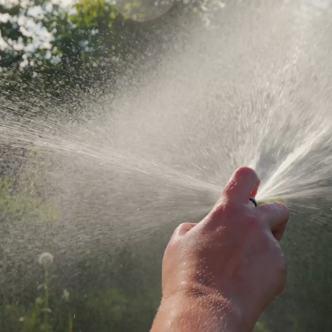 Close up of hand with garden hose watering garden and trees in garden