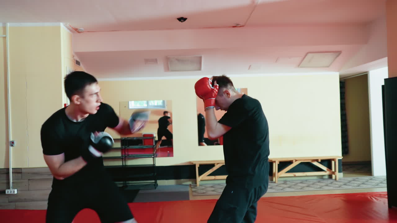 Karate practitioners in training stance inside martial arts gym, wearing gloves, preparing for sparring session, focusing on technique, concentration, movement during combat practice on red mat