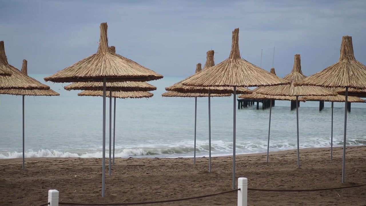 Ombrelloni di paglia su una spiaggia calma con onde leggere e un molo
