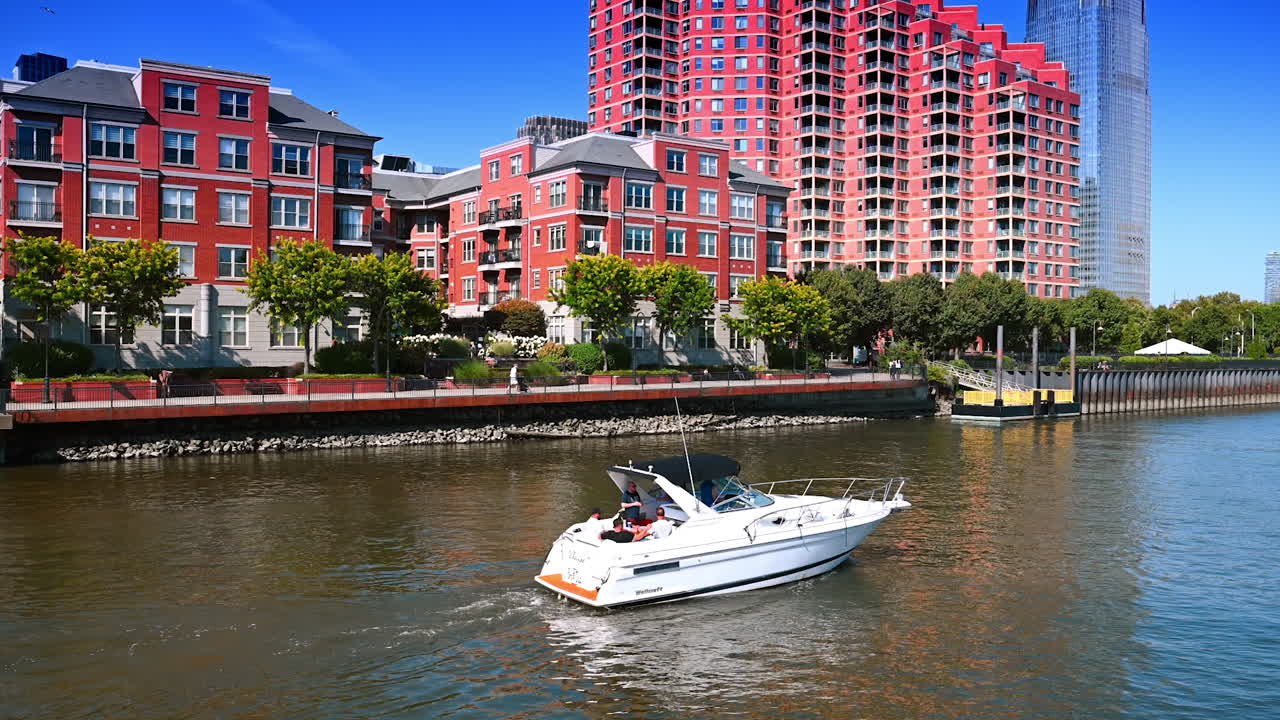 New Jersey, USA, 19 August 2025: Boat moves by the waterscape along the riverside with red facades. Boating on summer day in Jersey City, USA