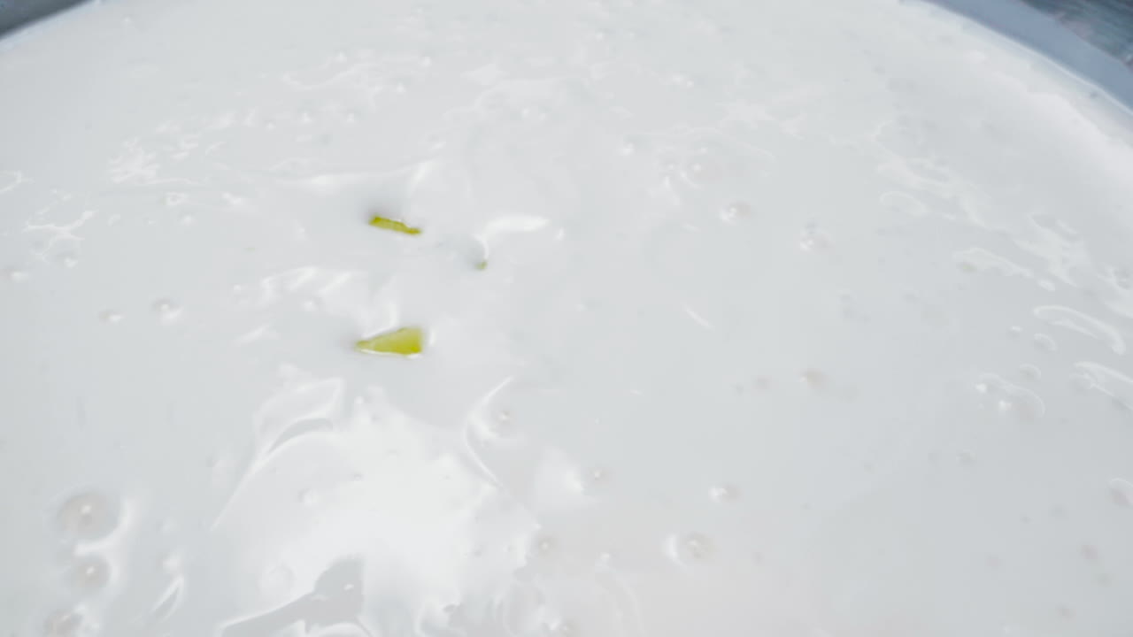 Slow motion close-up shot of fresh mango cubes falling gently into a bowl of smooth white yogurt. The vibrant yellow contrasts beautifully with the creamy white texture, creating a visually moment.