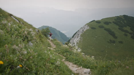 a hiker walking on a narrow path on a hill using hiking poles, walking towards the camera in the distance