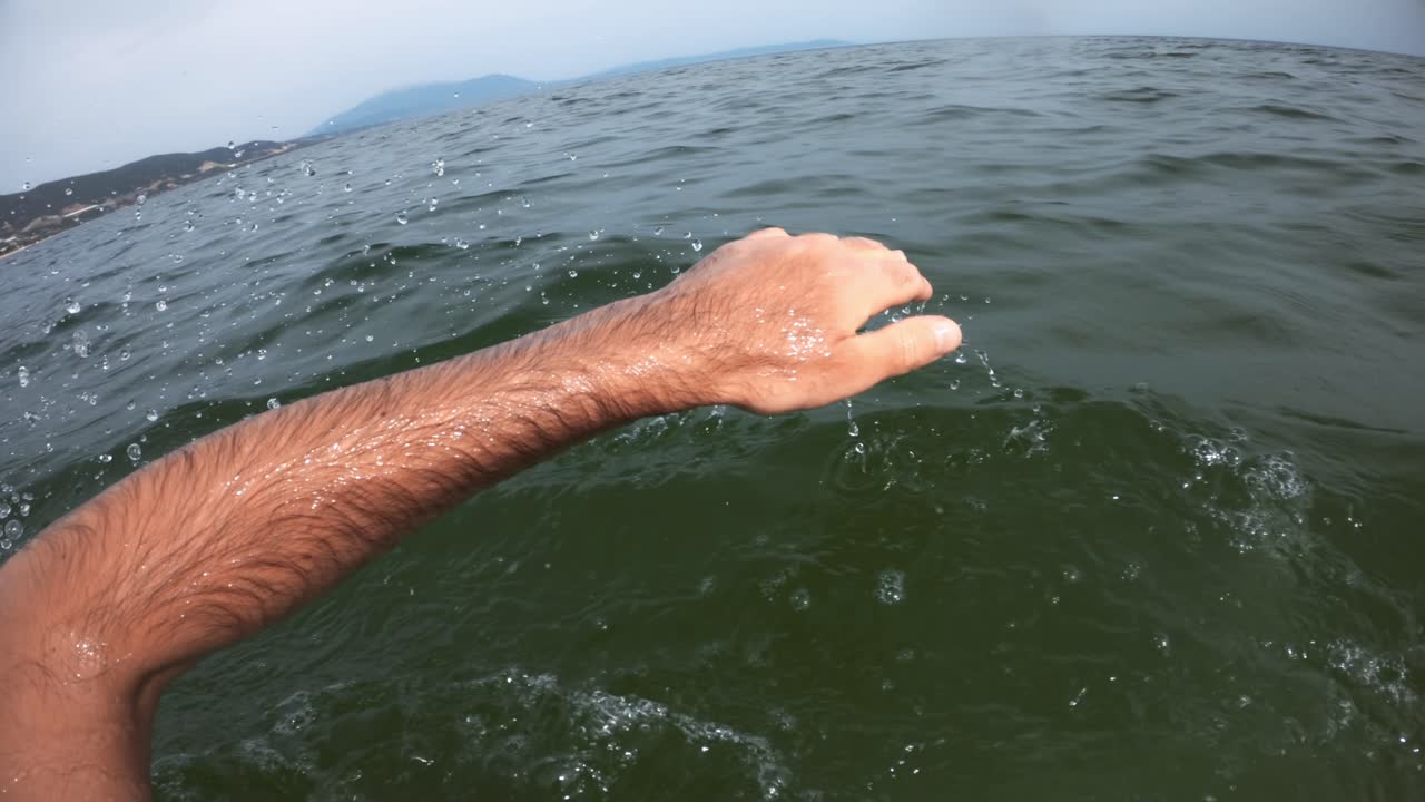 A man swimming in the dark water of a sea. Cloudy sky. First-person view, slow motion