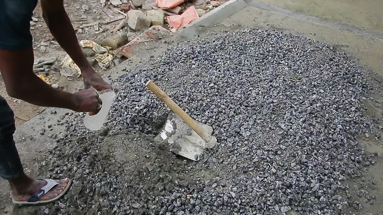 Indian mason worker pouring water over cement mix to ensure proper hydration for construction