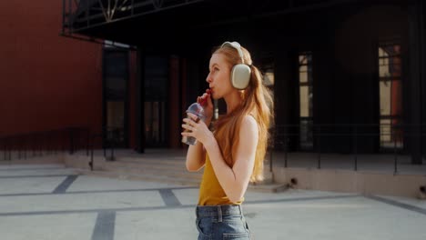 woman dancing and drinking outdoors with headphones