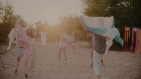 young friends swaying sarongs at beach during sunset