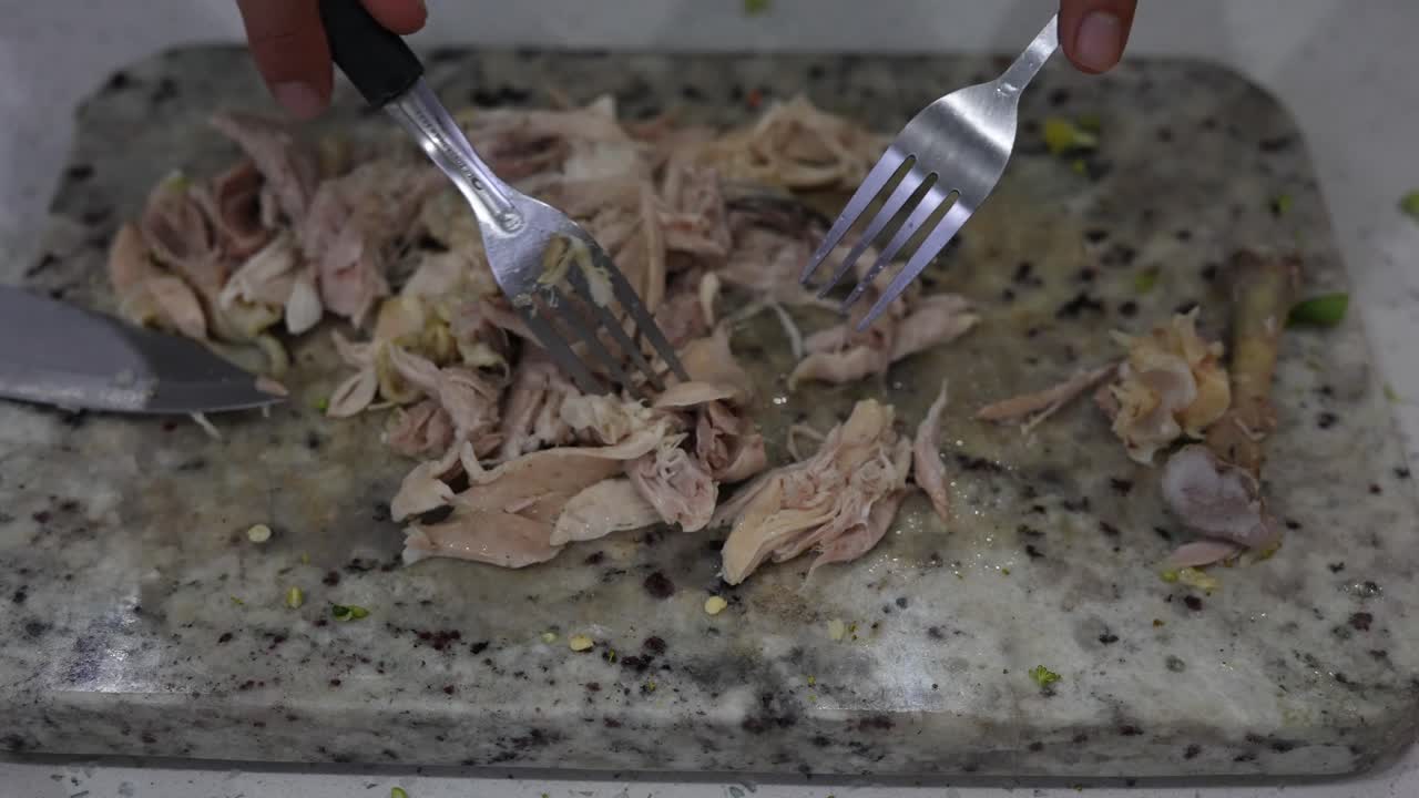 cortar pollo con un tenedor en una tabla de cortar en la cocina